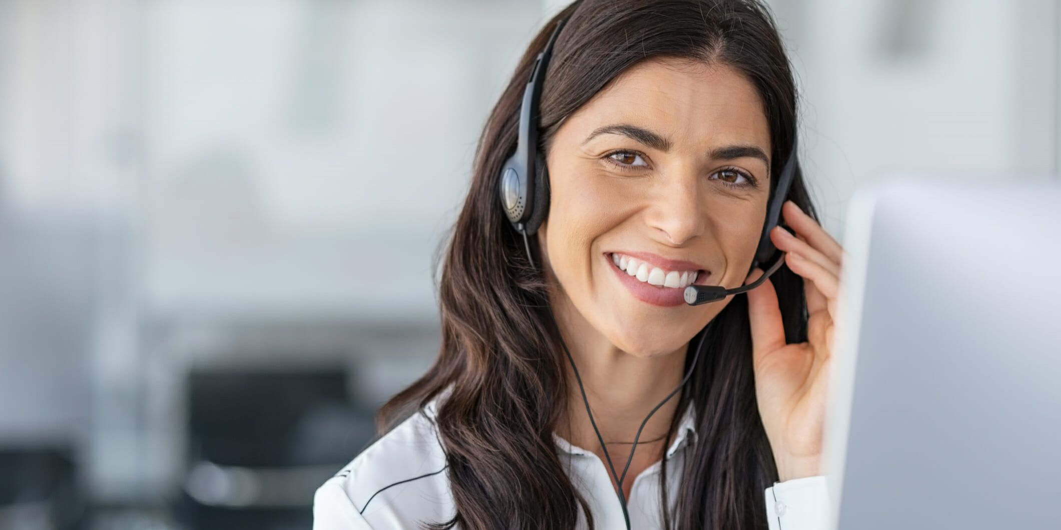 Call center agent with headset working on support hotline in modern office with copy space. Portrait of mature positive agent in conversation with customer over headset looking at camera. Consulting and assistance service customer support.